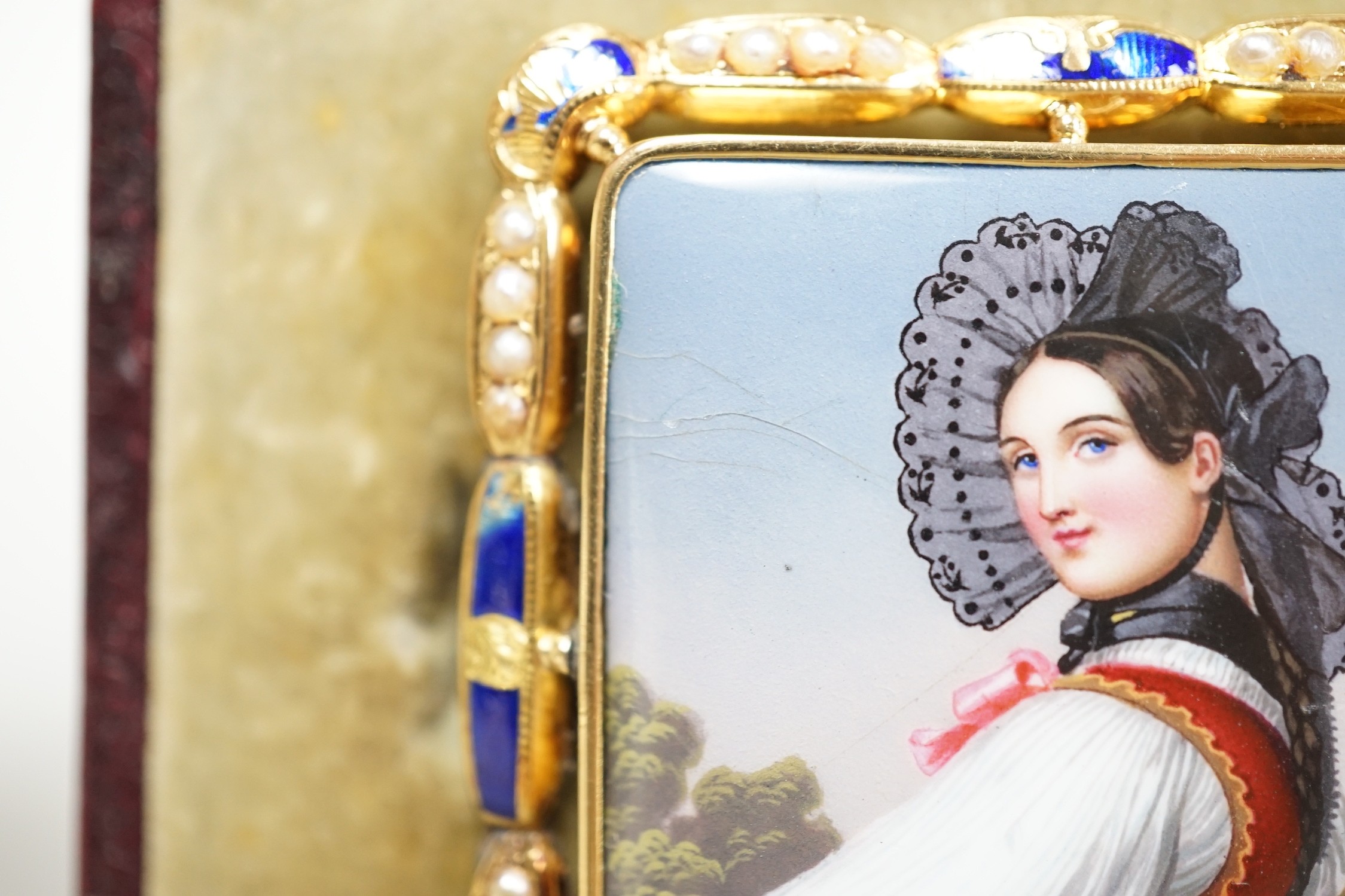 A cased Swiss? yellow metal, enamel and seed pearl mounted enamelled portrait brooch, 48mm, 13.8 grams.